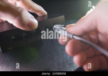 Close-up Hand holding ethernet cable on network switches background. Home network concept. Stock Photo