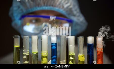 Scientist analyzing reaction in test tubes with multicolored bubbling liquids Stock Photo