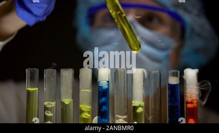 Chemist checking sediment in tube with yellow liquid, substances emitting smoke Stock Photo