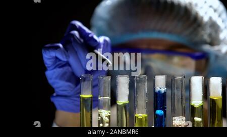 Lab worker analyzing test reaction pointing by pen at tube on black background Stock Photo