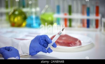 Scientist holding syringe with antibiotic near meat sample, experiments, gmo Stock Photo