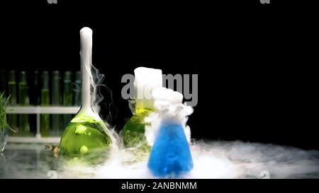 Multicolored substances in flasks bubbling and emitting smoke in darkness, test Stock Photo