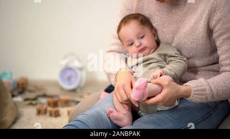 Mommy putting pink socks on adorable baby girl, newborn clothing and accessories Stock Photo