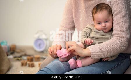 Woman dressing little cute infant girl in pink socks, natural clothing materials Stock Photo