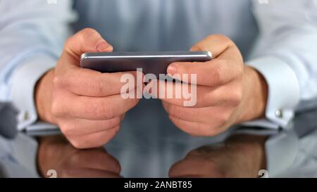 Male hands playing game on smartphone, fingers touching screen, gadget addiction Stock Photo
