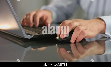 Stock exchange broker working on laptop holding computer mouse, scrolling site Stock Photo