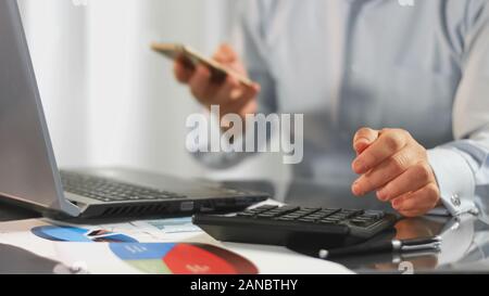 Financial expert calculating taxes holding smartphone in hand, office work Stock Photo