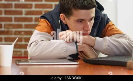Young sad male searching job online using laptop, feeling bored, unemployment Stock Photo