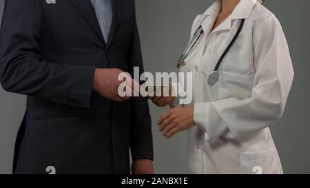 Rich male patient gives money to doctor, expensive health insurance, bribe Stock Photo