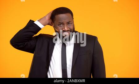 Embarrassed african-american male in suit scratching head, making hard decision Stock Photo