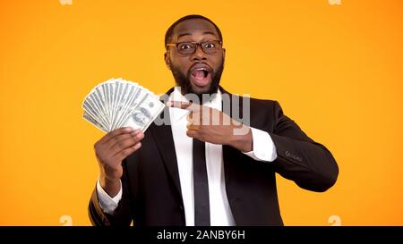 Happy successful african-american man in suit pointing at bunch of dollar cash Stock Photo