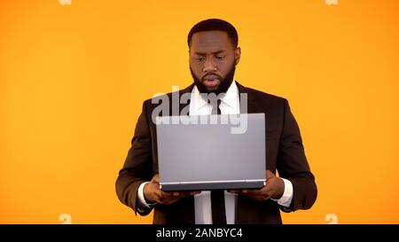 African-american male reading news on laptop and frowning, embarrassing news Stock Photo