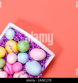 Multicolor eggs in a white tray. Creative Easter concept. Modern solid pink background. Square. Living coral theme - color of the year 2019 Stock Photo