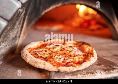 Baked tasty margherita pizza in Traditional wood oven in Naples restaurant, Italy. Original neapolitan pizza. Red hot coal. Stock Photo