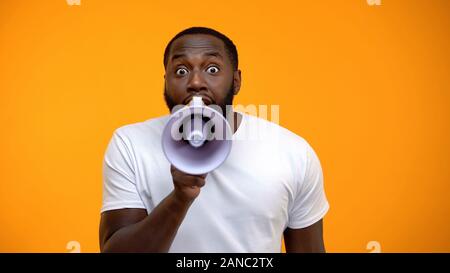 Frightened black man screaming in megaphone, spreading information, awareness Stock Photo