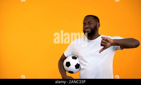 African-American man playing with soccer ball and showing thumbs down, losing Stock Photo
