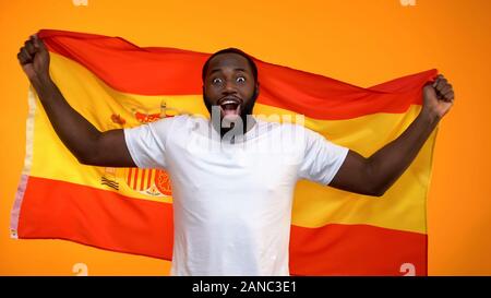Cheerful black sport fan holding Spanish flag cheering for national team victory Stock Photo