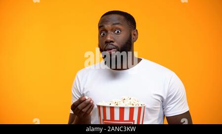 Excited African-American male with popcorn watching interesting TV program Stock Photo