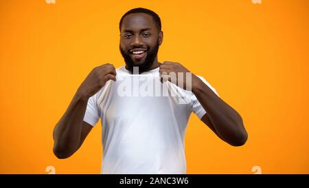 Smiling black man showing his white T-shirt isolated on yellow background Stock Photo