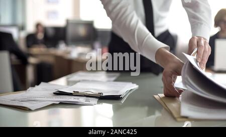 HR officer searching resume in stack of papers, preparing documents for meeting Stock Photo