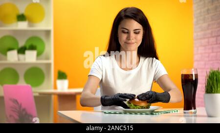 Pretty lady in black rubber gloves taking tasty cheeseburger, sitting in bistro Stock Photo