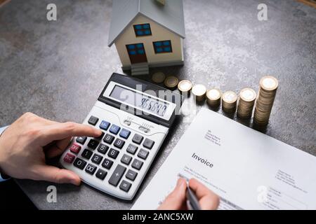 Businessman With Coins And House Model Using Calculator Stock Photo