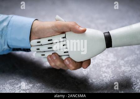 Close-up Of Digital Generated Human Hand And Business Man Shaking Hands Against Grey Background Stock Photo