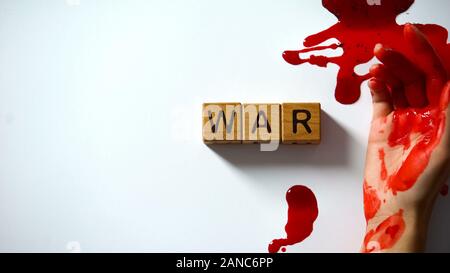 War word made of wooden cubes, bleeding hand on table, political conflict Stock Photo