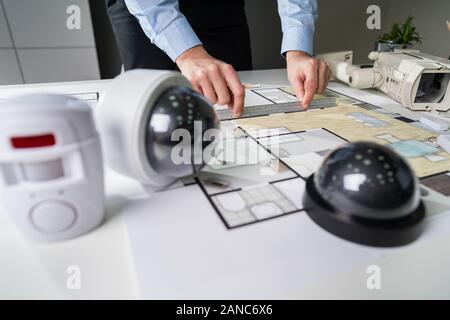Close-up Of An Architect's Hand Drawing Blueprint With Security Equipment On Desk Stock Photo