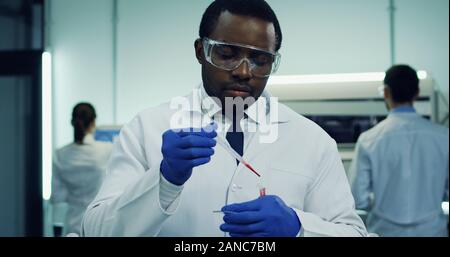 Portrait of the African American handsome male laboratory worker making a blood test in the glass tube in hands. Close up. Stock Photo