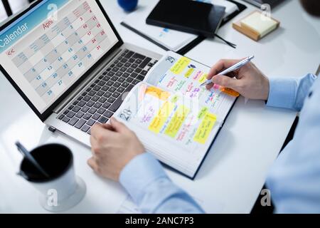 Close-up Of Businessman Writing Schedule In Calendar Diary On Desk Stock Photo