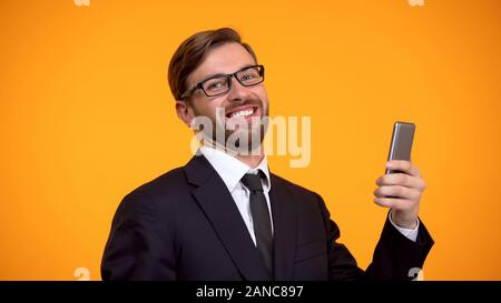 Happy man sincerely smiling holding smartphone in hand, favorable crediting, app Stock Photo
