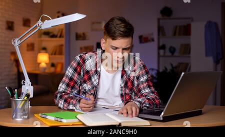 Student reading task in book and writing answer down to copybook, homework Stock Photo