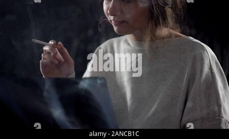 Young female smoking cigarette looking at lungs x-ray image, incurable disease Stock Photo