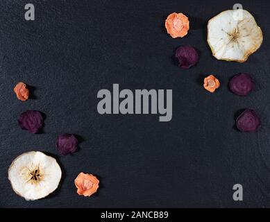 Dried carrot, beetroot and apple chips on a black stone background. Organic natural food. Top view, flat lay. Copy space. Stock Photo