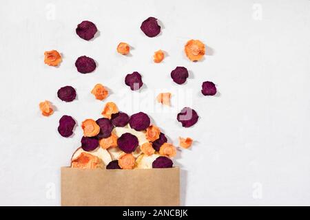 Dried carrot, beet, apple chips in a paper bag on a white concrete background. Organic natural food. Top view, flat lay. Stock Photo