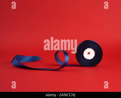 spool of twisted dark blue silk shiny ribbon on a red background ...