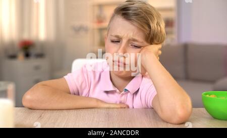 Sad schoolboy sitting at table, refusing to eat breakfast, childhood nutrition Stock Photo