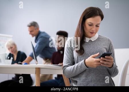 Distracted Businesswoman Using Mobile Phone In Meeting Stock Photo