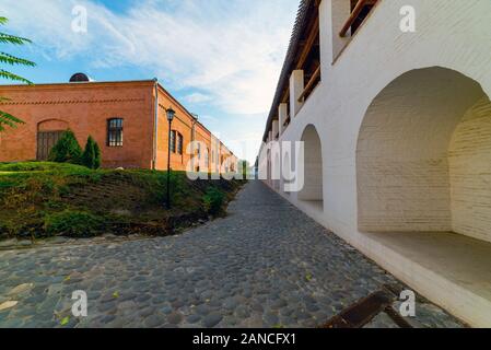 White stone wall of the courtyard with large arches and a wooden roof along the road with masonry in cloudy weather with blue clouds. Historical and a Stock Photo