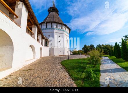 White stone wall of the courtyard with large arches and a wooden roof along the road with masonry in cloudy weather with blue clouds. Historical and a Stock Photo