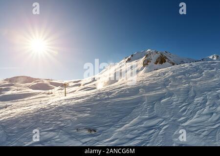 Scenic valley of hilghland alpine mountain winter resort on bright sunny day. Wintersport scene with people enjoy skiing and snowboarding on groomed Stock Photo