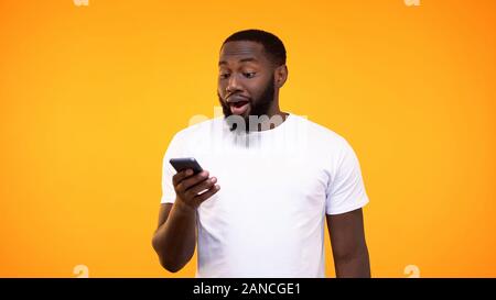 Surprised black man using smartphone application against yellow background Stock Photo