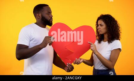 Offended boyfriend and girlfriend holding paper heart parts, relations conflict Stock Photo
