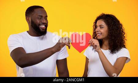 Happy young couple holding red paper heart and smiling, true love and care Stock Photo