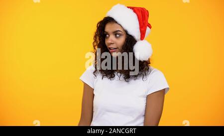 Curious curly-haired female in santa hat and white t-shirt on bright background Stock Photo
