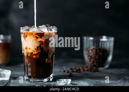 Milk Being Poured Into Iced Coffee on a dark table Stock Photo