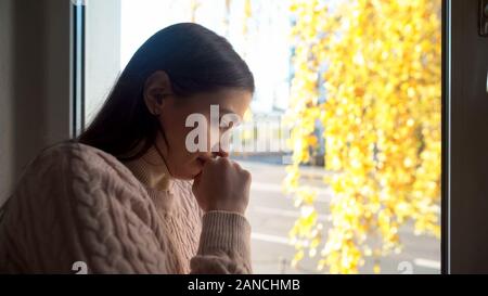 Young crying woman looking through window, life and health problems, depression Stock Photo