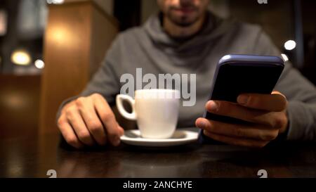 Upset man sitting in cafe and using smartphone, reading bad news message sadness Stock Photo