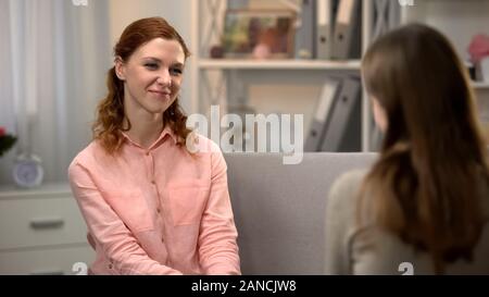Pretty young woman smiling to female friend, talking on sofa, companionship Stock Photo